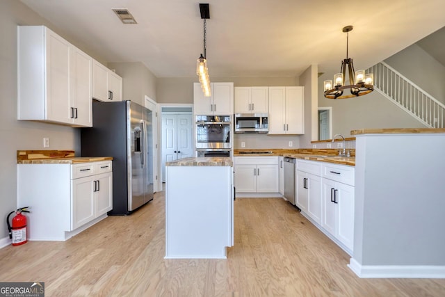 kitchen featuring hanging light fixtures, stainless steel appliances, and white cabinets