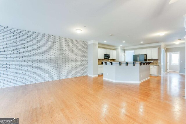 unfurnished living room featuring brick wall and light wood-type flooring