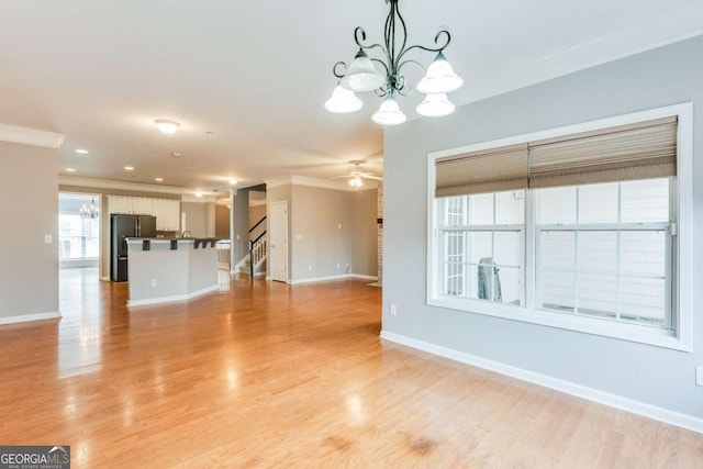 unfurnished living room featuring crown molding, ceiling fan with notable chandelier, and light hardwood / wood-style floors