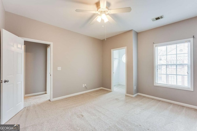 unfurnished bedroom with a spacious closet, light colored carpet, and ceiling fan