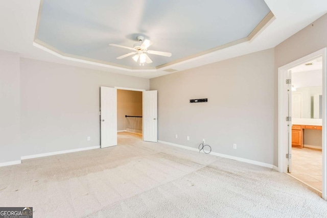 spare room with ceiling fan, a raised ceiling, and light carpet