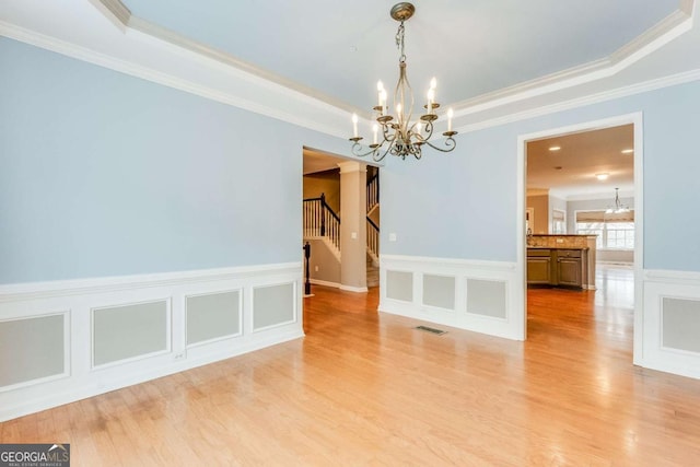 unfurnished room with an inviting chandelier, a tray ceiling, light hardwood / wood-style flooring, and ornamental molding