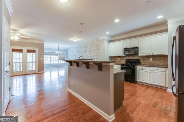 kitchen featuring a center island with sink, white cabinets, a kitchen bar, and black appliances