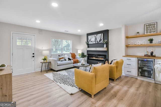 living room with wine cooler, bar area, a fireplace, and light hardwood / wood-style flooring