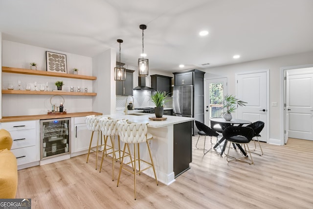 kitchen featuring wine cooler, a kitchen bar, hanging light fixtures, kitchen peninsula, and wall chimney exhaust hood