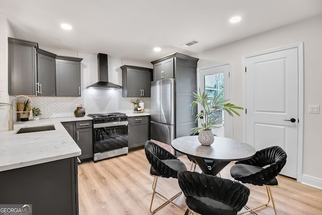 kitchen with sink, gray cabinetry, stainless steel fridge, gas range oven, and wall chimney range hood