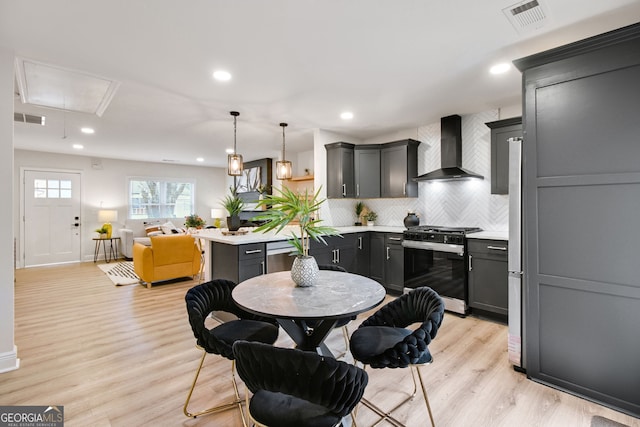 kitchen featuring gas range, pendant lighting, light hardwood / wood-style floors, and wall chimney range hood