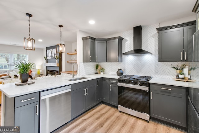 kitchen featuring range with gas stovetop, dishwasher, sink, hanging light fixtures, and wall chimney range hood