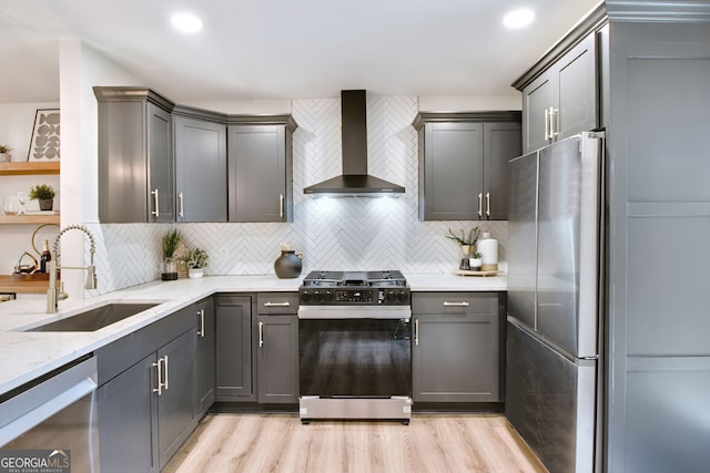 kitchen with sink, light hardwood / wood-style floors, wall chimney exhaust hood, and appliances with stainless steel finishes