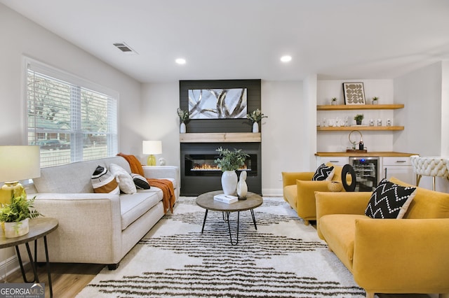 living room featuring a fireplace, bar area, beverage cooler, and light hardwood / wood-style flooring