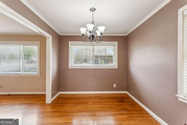 empty room with a notable chandelier, crown molding, and wood-type flooring