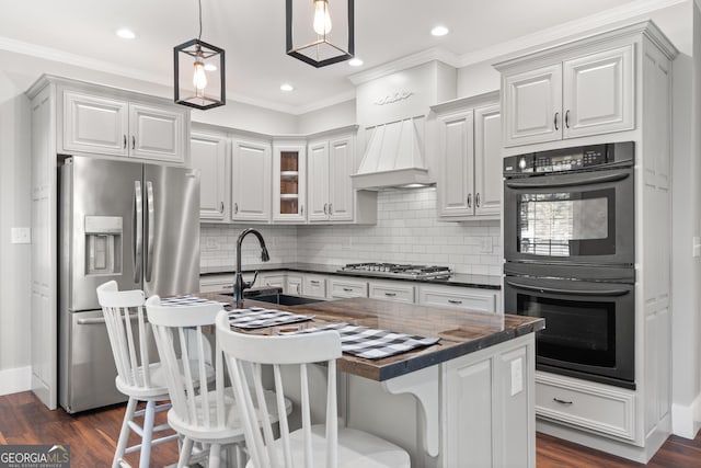 kitchen featuring sink, premium range hood, appliances with stainless steel finishes, hanging light fixtures, and a center island