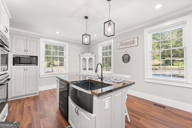 kitchen with decorative light fixtures, black appliances, white cabinets, and a center island with sink