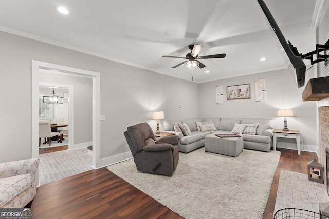 living room with crown molding, ceiling fan with notable chandelier, hardwood / wood-style floors, and a fireplace