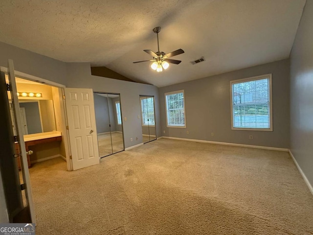 unfurnished bedroom with vaulted ceiling, ensuite bathroom, carpet, multiple closets, and a textured ceiling