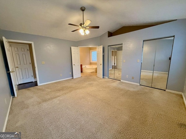 unfurnished bedroom with lofted ceiling, ceiling fan, carpet, connected bathroom, and two closets