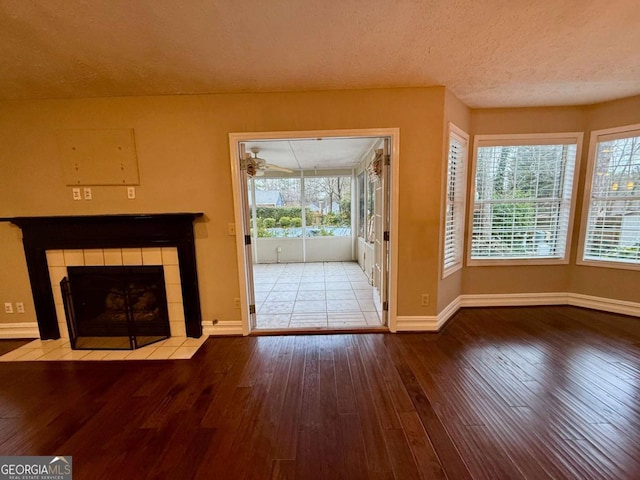 unfurnished living room featuring a tiled fireplace, wood-type flooring, a wealth of natural light, and a textured ceiling