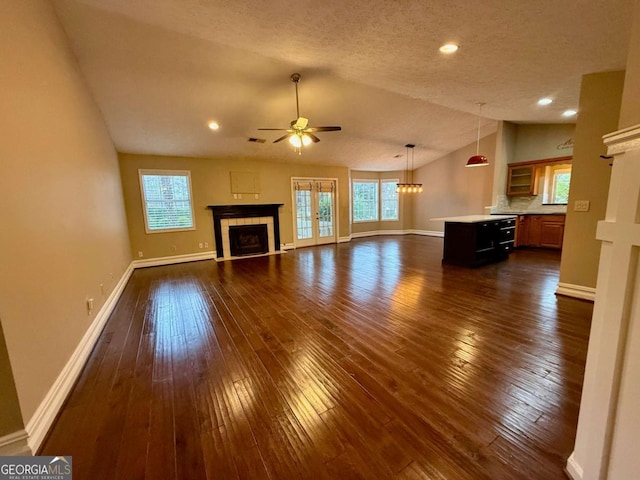 unfurnished living room with dark wood-type flooring, a healthy amount of sunlight, lofted ceiling, and a tile fireplace