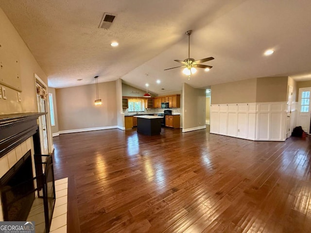 unfurnished living room with lofted ceiling, dark hardwood / wood-style flooring, a tiled fireplace, ceiling fan, and a textured ceiling