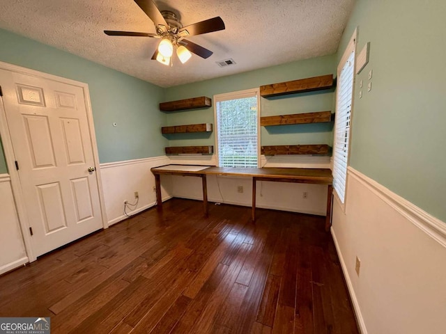 unfurnished office featuring dark hardwood / wood-style floors, built in desk, a textured ceiling, and ceiling fan