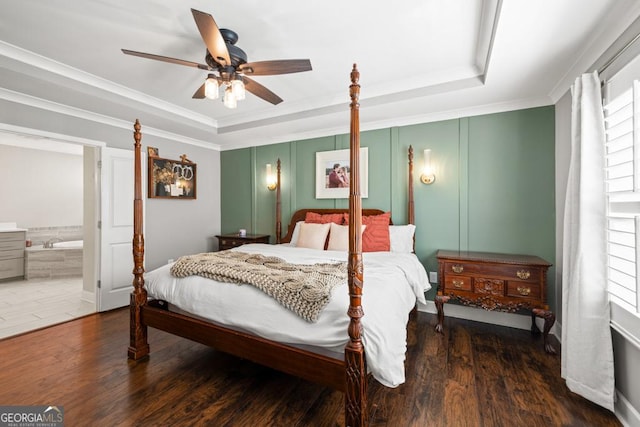 bedroom with ensuite bath, dark wood-type flooring, ornamental molding, and a raised ceiling