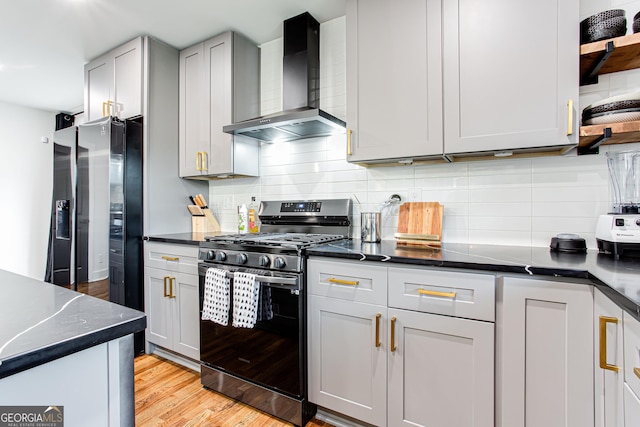 kitchen featuring appliances with stainless steel finishes, tasteful backsplash, dark stone countertops, light hardwood / wood-style floors, and wall chimney range hood