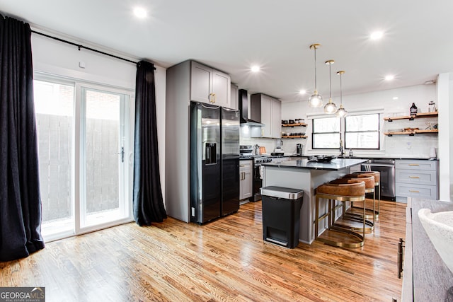 kitchen with appliances with stainless steel finishes, gray cabinetry, a kitchen island, a kitchen bar, and wall chimney exhaust hood