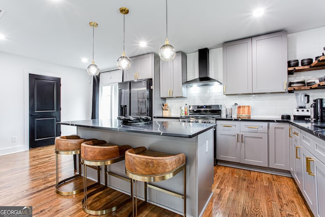 kitchen featuring appliances with stainless steel finishes, gray cabinetry, wall chimney range hood, and a kitchen breakfast bar