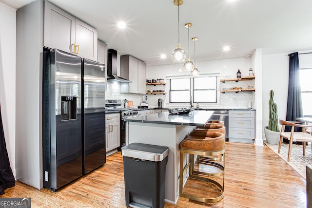 kitchen with wall chimney exhaust hood, gray cabinetry, light hardwood / wood-style flooring, a kitchen island, and stainless steel appliances