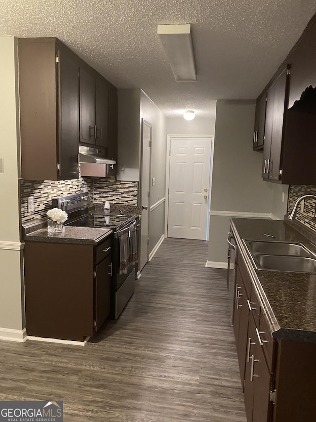 kitchen featuring electric stove, under cabinet range hood, dark countertops, a sink, and a textured ceiling