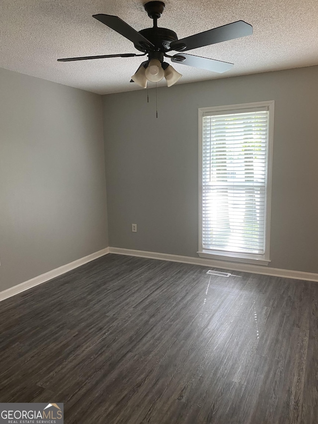 spare room with a textured ceiling, ceiling fan, visible vents, dark wood-style floors, and baseboards