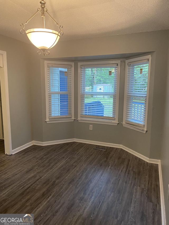 unfurnished dining area featuring a textured ceiling, dark wood finished floors, and baseboards