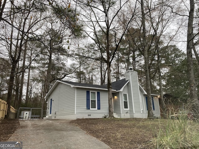 view of front of home featuring concrete driveway, fence, crawl space, and a chimney
