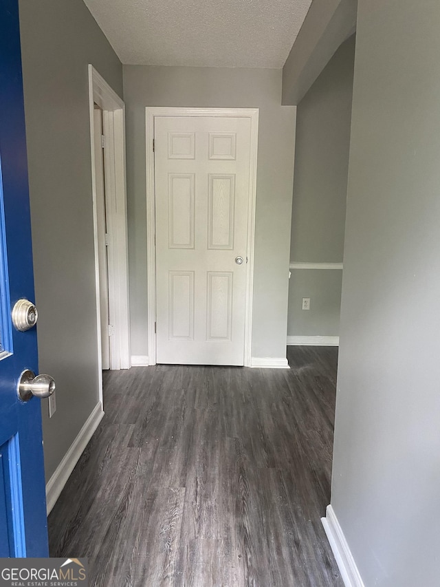 hall featuring a textured ceiling, wood finished floors, and baseboards