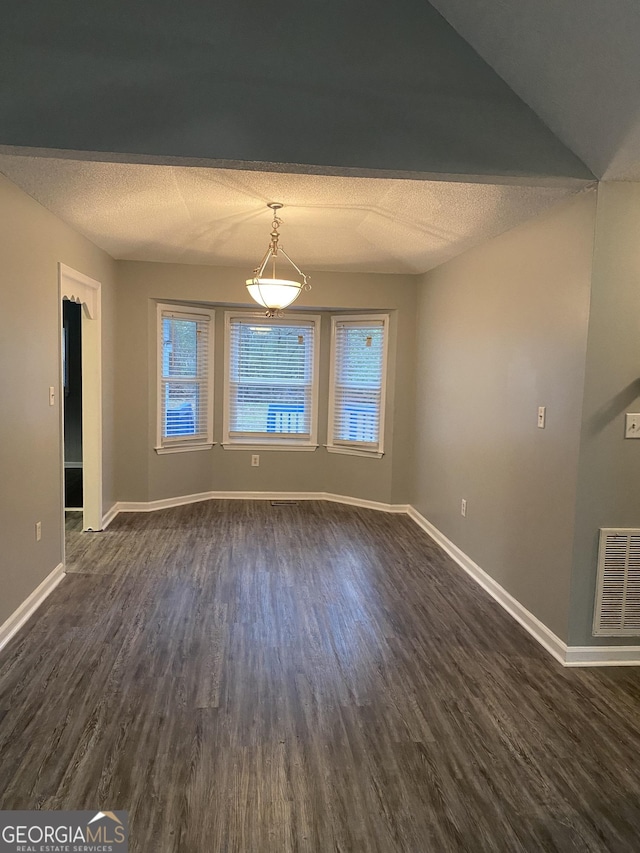 unfurnished dining area with a textured ceiling, visible vents, dark wood-style flooring, and baseboards