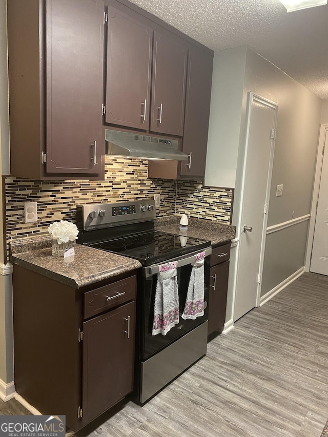 kitchen featuring electric stove, light wood-style floors, under cabinet range hood, dark countertops, and a textured ceiling