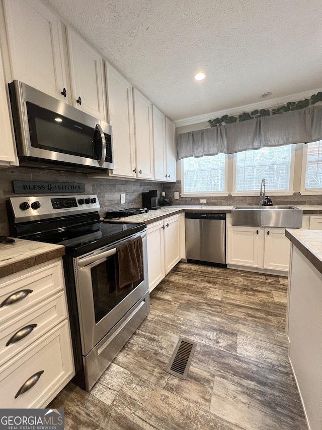 kitchen featuring dark hardwood / wood-style floors, sink, white cabinets, backsplash, and stainless steel appliances