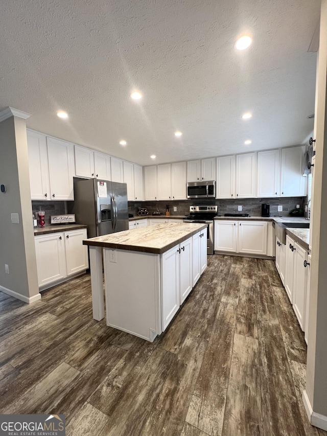 kitchen with dark wood-type flooring, appliances with stainless steel finishes, backsplash, and white cabinets