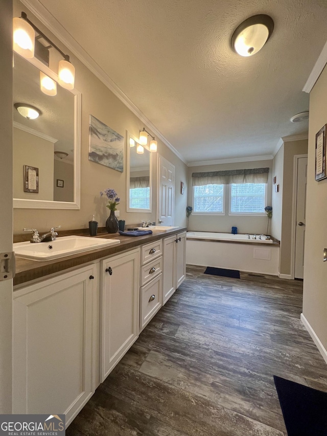 bathroom with a tub to relax in, crown molding, a textured ceiling, vanity, and hardwood / wood-style floors