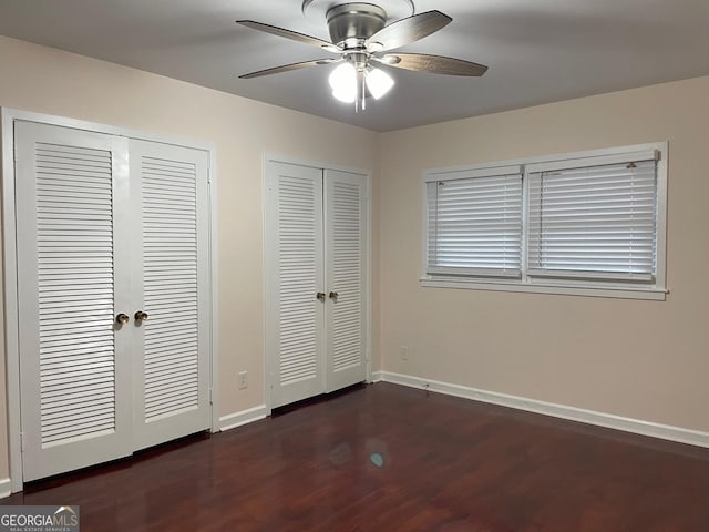 unfurnished bedroom featuring dark wood-type flooring, ceiling fan, and two closets