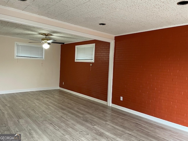 spare room featuring hardwood / wood-style floors, ornamental molding, ceiling fan, and brick wall