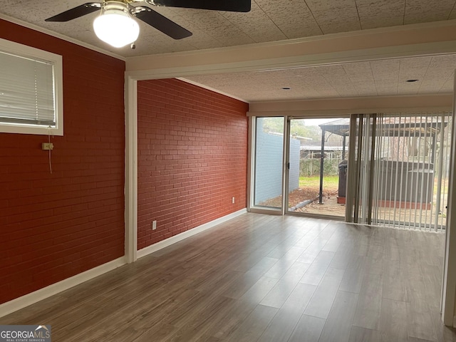 unfurnished room with wood-type flooring, ornamental molding, ceiling fan, and brick wall