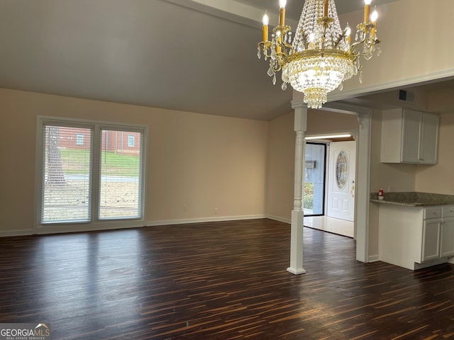 unfurnished living room featuring decorative columns, lofted ceiling, dark wood-type flooring, and a chandelier