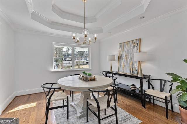 dining space featuring a tray ceiling, ornamental molding, a chandelier, and light hardwood / wood-style floors