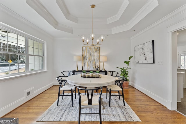 dining area featuring a raised ceiling, light wood-type flooring, crown molding, and a notable chandelier