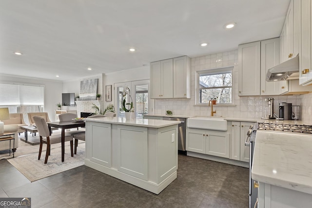 kitchen featuring stainless steel appliances, a kitchen island, sink, light stone counters, and white cabinets