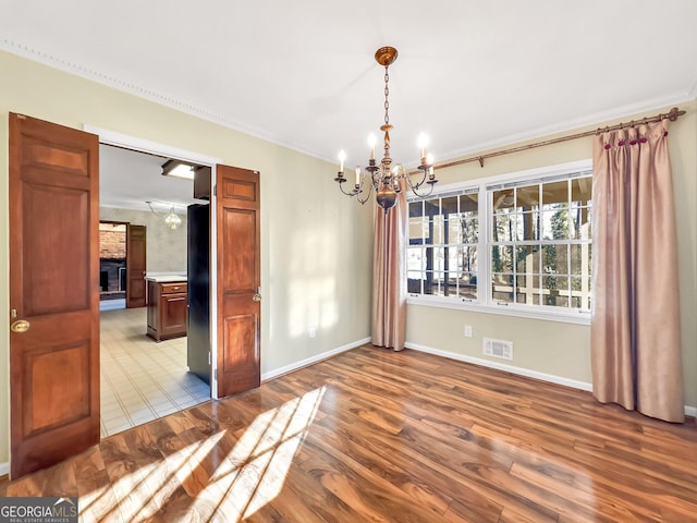 unfurnished dining area with ornamental molding, a fireplace, a chandelier, and light hardwood / wood-style floors