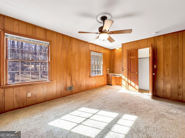 carpeted spare room with wooden walls and ceiling fan