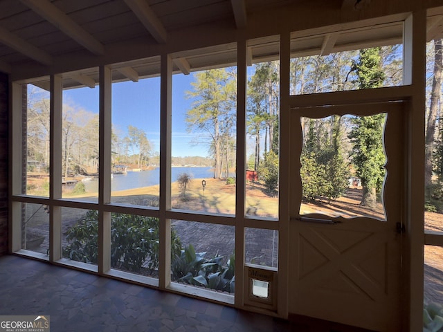 unfurnished sunroom featuring a water view, beamed ceiling, and a wealth of natural light