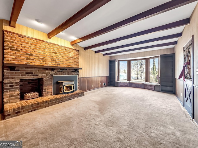 unfurnished living room with beamed ceiling, a brick fireplace, carpet, and wood walls